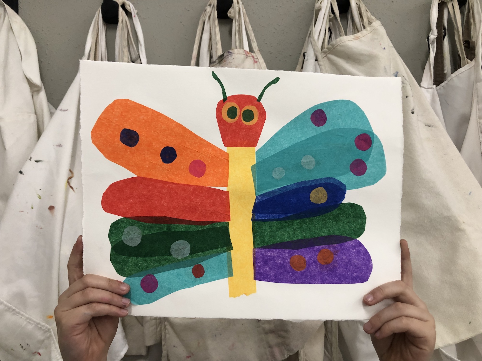 a child's hands holding a colorful collage of a butterfly 