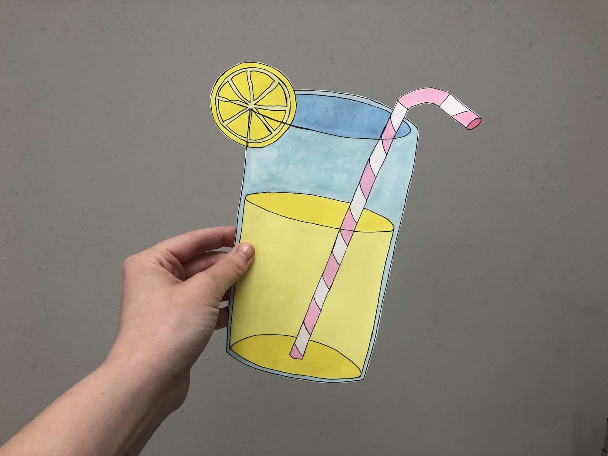 hand holding a cut out watercolor painting of a glass of lemonade 