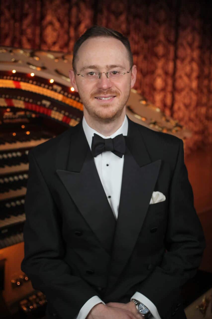 Man with glasses in a suit standing in front of an organ